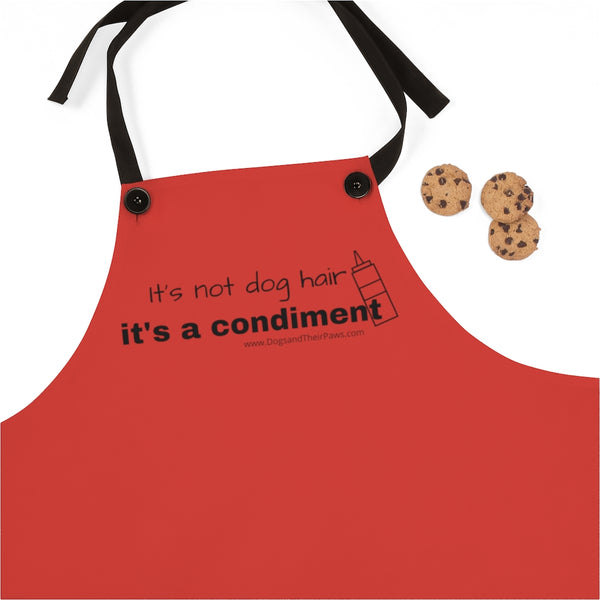 It's a Condiment Ketchup Apron - Image of ketchup colored red apron with saying It's not dog hair it's a condiment with an outline of a condiment  bottle with 3 chocolate chip cookies. The black neck time straps are attached with black buttons.