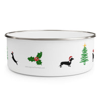 Dogs Holiday Cheer Enamel Bowl - White bowl with stainless steel rim decorated with a dog jumping towards the edge of the bowl, a holy with a paw print as a berry, A silhouette of a dachshund wearing a santa hat facing a green line shaped Christmas tree with another dog facing the tree only partially visible on the side of the bowl.  