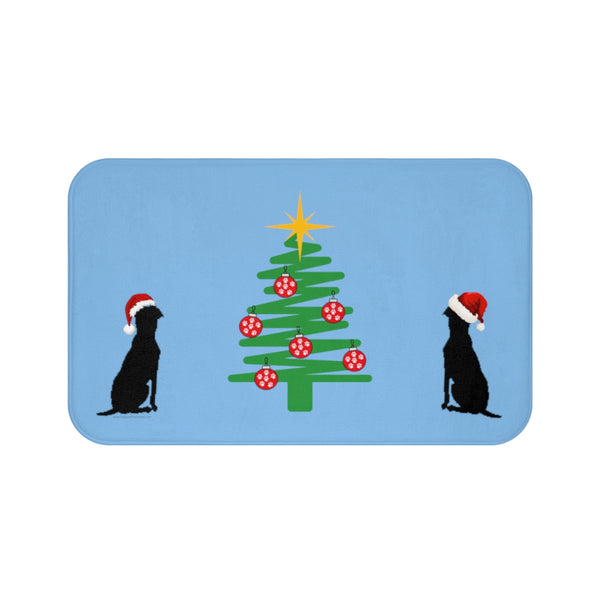 Image Description - Light blue bathmat with two dogs  with Santa hats sitting on opposite sides of a Christmas tree decorated with Red ornaments covered in paw prints and topped with a yellow star. 