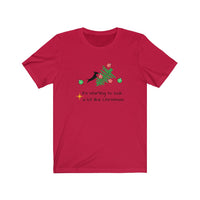 Tumbled Christmas Tree Unisex Jersey Tee - Red t-shirt with a picture of a line Christmas tree on it's side and a black silhouette dachshund jumping on the tree with  several red and green ornaments falling off the tree 