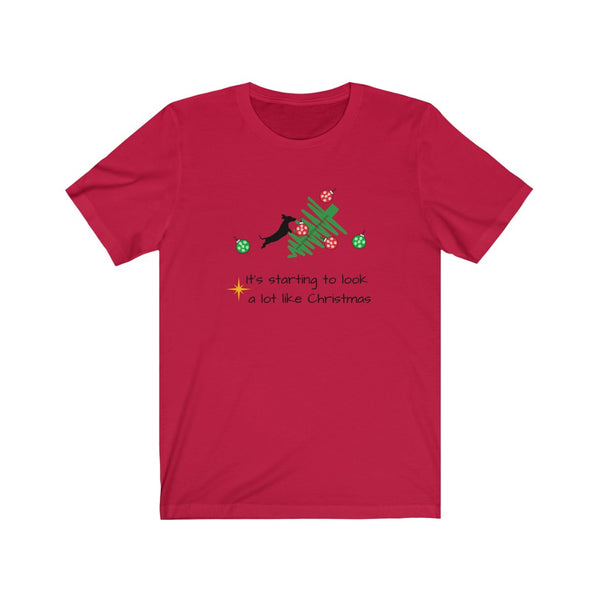 Tumbled Christmas Tree Unisex Jersey Tee - Red t-shirt with a picture of a line Christmas tree on it's side and a black silhouette dachshund jumping on the tree with  several red and green ornaments falling off the tree 