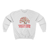 Image Description: White crew neck sweatshirt. There are orange and red maple leaves  on a brown tree trunk with a small black dog walking beside the tree trunk.  The www.DogsandTheirPaws.com url is under the tree.  The phrase, "Leaves are falling.  Autumn is calling." is below the image of the tree is in red.  