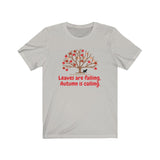 Image Description: Light Grey crew neck t-shirt. Orange and red maple leaves  on a brown tree trunk with a small black dog walking beside the tree trunk.  The www.DogsandTheirPaws.com url is under the tree.  The phrase, "Leaves are falling.  Autumn is calling." is below the image of the tree is in red.  