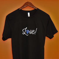 Love Script Paw Print Unisex Jersey Tee - Black t-shirt with the word Love! in white cursive script on the front of the shirt. The O from the word love is a royal blue paw print hanging from a wood hanger against an orange background.