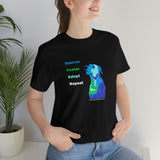 Blue Rescue, Foster, Adopt, Repeat Tee - Image of a female model standing in front of a green plant wearing a Black short sleeve jersey t-shirt with a multi-colored dog (terrier/mutt) head and chest looking up next to words in colors that match the dog - Rescue (blue) Foster (green) Adopt (teal) Repeat (white) 